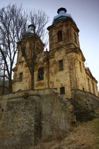 Polorozpadlé přístupové schodiště. Proti původním plánům získal kostel mohutné dvouvěžové průčelí. Fasáda kostela ještě čeká na opravu, vnitřek kostela je už celkem v pořádku.